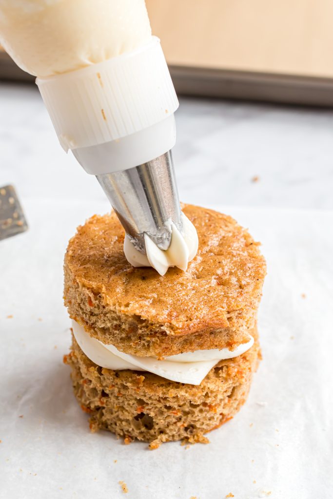 A photo of a double layer carrot cake with a cream cheese frosting swirl being piped on top