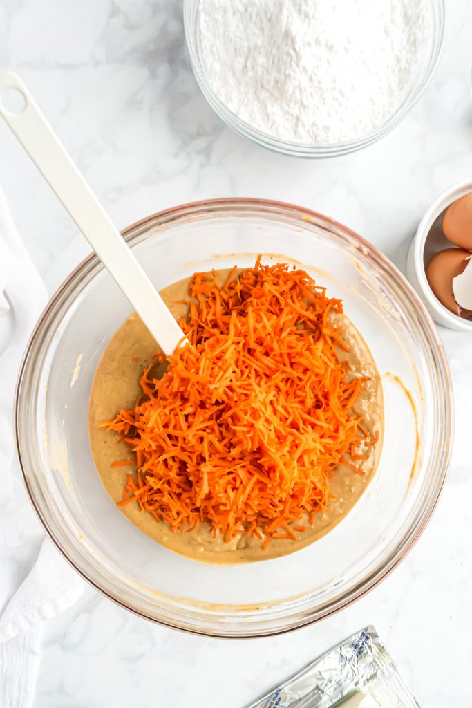 An overhead photo of shredded carrots on top of the batter in the mixing bowl