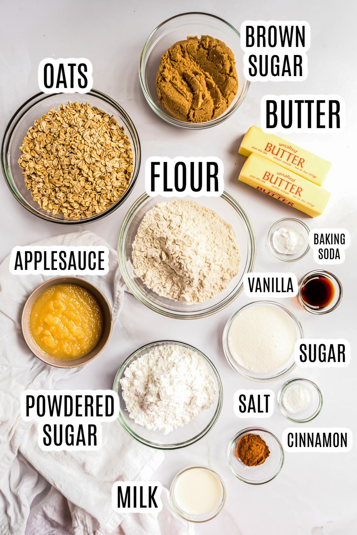 All the ingredients needed to make the oatmeal cookies without egg including: brown sugar, butter, oats, flour, applesauce, baking soda, vanilla, granulated sugar cinnamon, milk, and powdered sugar.