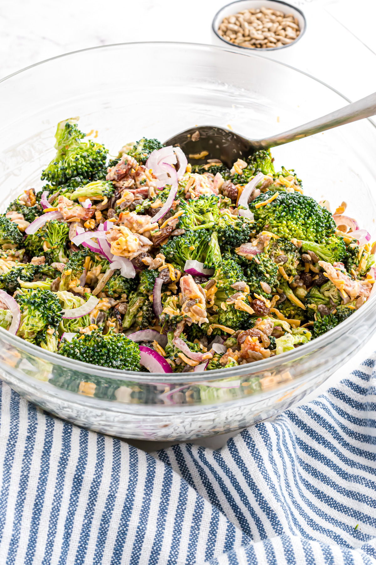 A large serving bowl filled with broccoli salad and a large serving spoon sticking out of the salad.