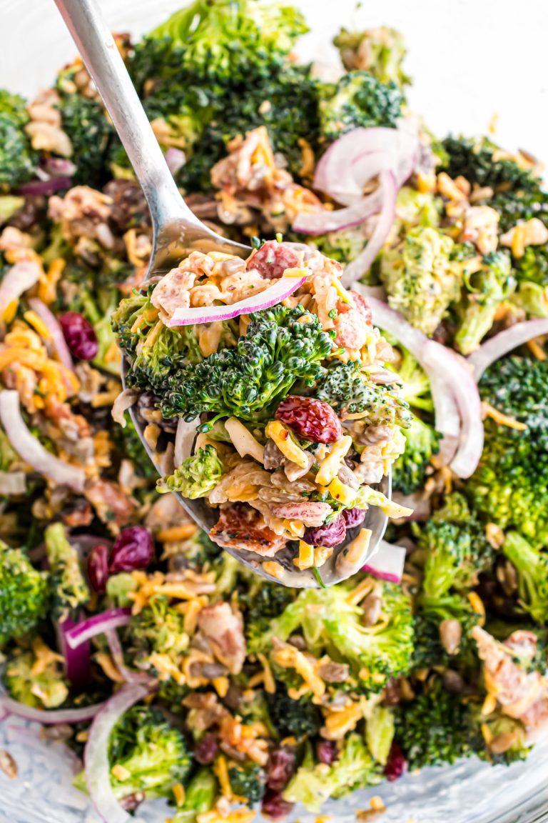 A spoonful of broccoli salads with craisins hovering over a glass bowl full of the salad.