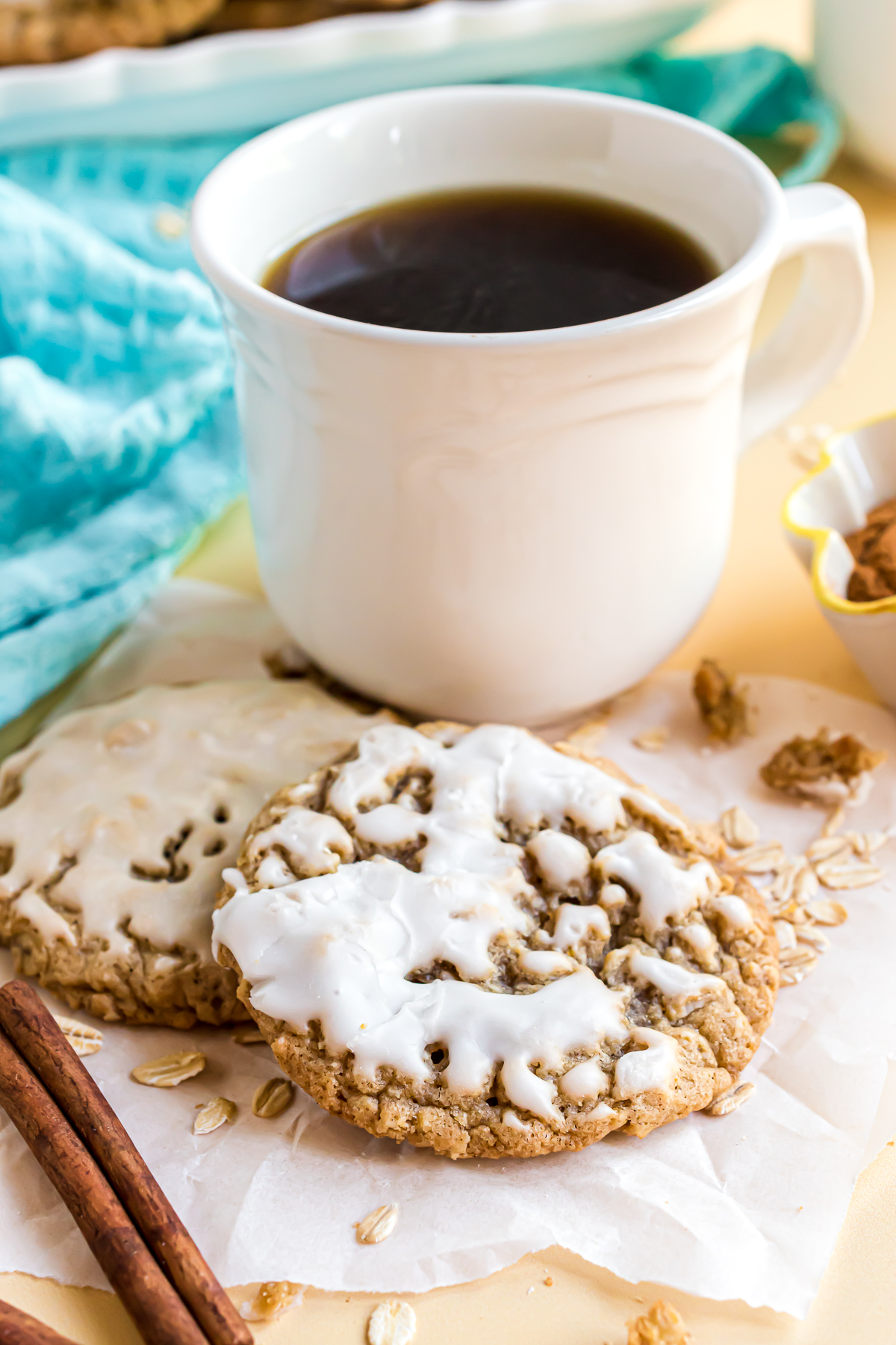 Two oatmeal cookies overlapping and laying on a piece of crumpled parchment paper in front of a coffee cup.