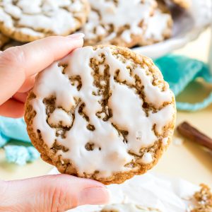 An iced oatmeal cookie being held by a hand showing the tops of the cookie and all the white icing filling the cracks and bumps on the surface of the cookie.