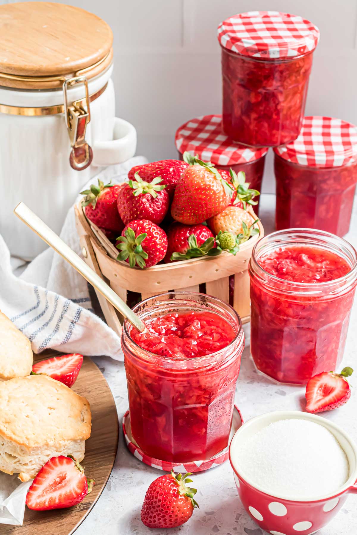 A jar of opened strawberry freezer jam with a serving spoon sticking out of it,