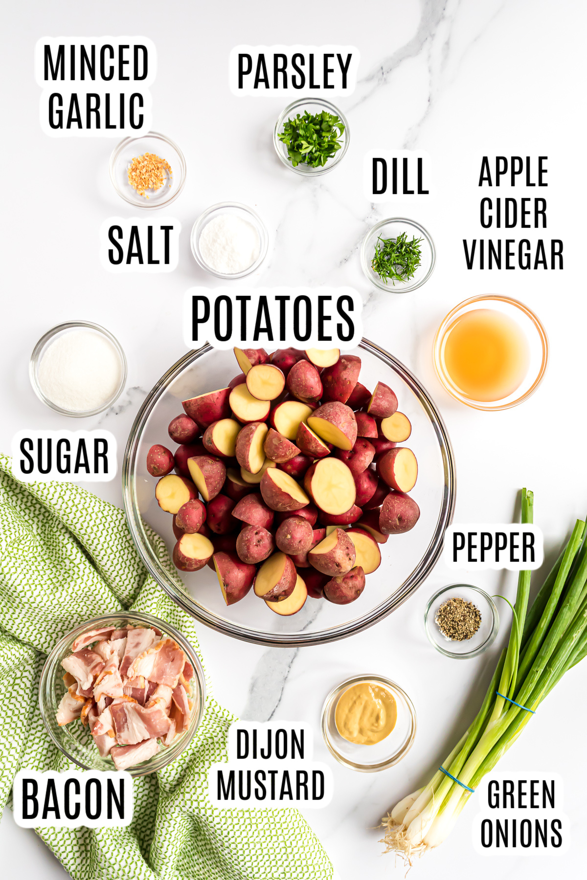 All the ingredients needed to make the dish, including baby red potatoes, minced garlic, parsley, salt, dill, apple cider vinegar, sugar, pepper, green onions, dijon mustard, and bacon.