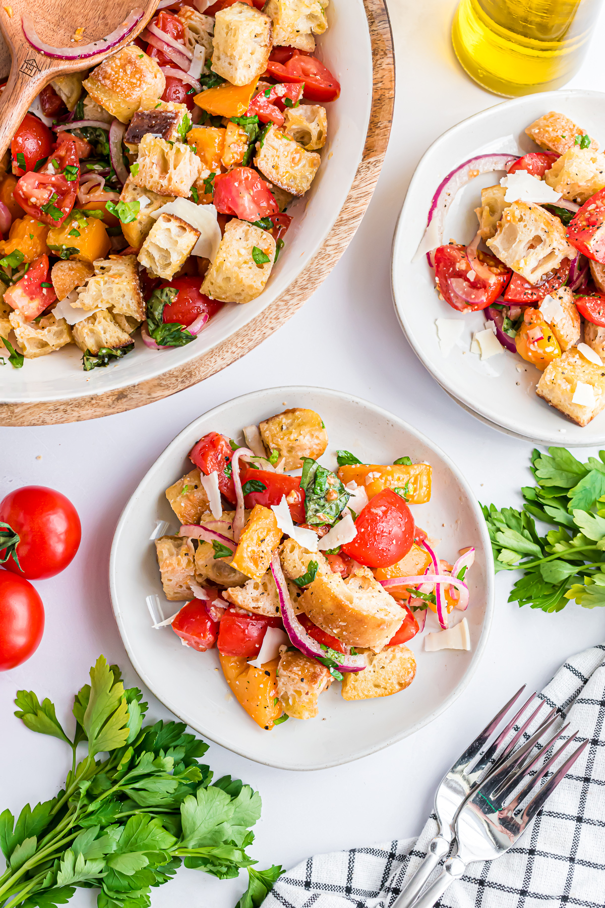 A serving bowl filled with Panzanella and 2 smaller salad plates with the salad waiting to be eaten.