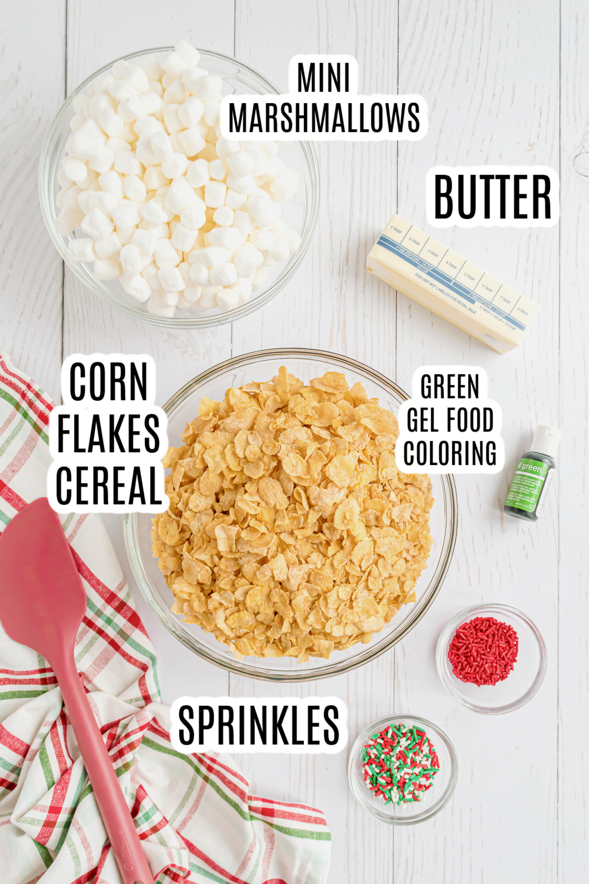 All of the ingredients needed to make the Christmas wreath cookie recipe including butter, mini marshmallows, corn flakes cereal, green food coloring and sprinkles.