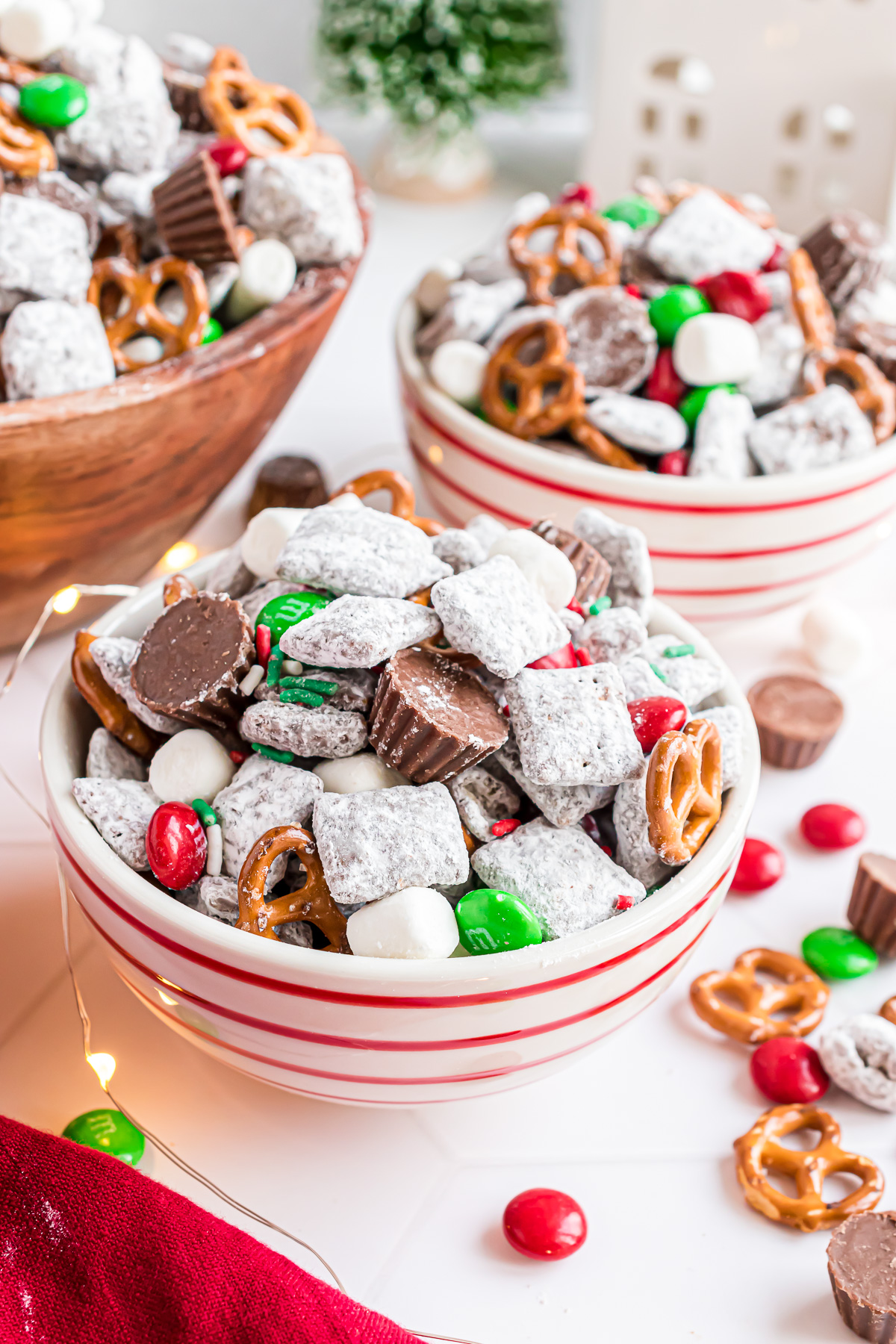 A small serving bowl of Reindeer mix surrounded by white holiday lights and red and green m&m candies.