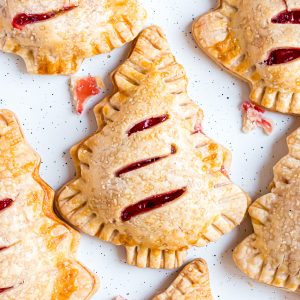 A cherry hand pie laying flat on a baking sheet surrounded by other pies.