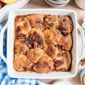 An square baking dish with a baked peach cobbler. The top of the dessert is a golden brown biscuit topping sprinkled with cinnamon sugar.