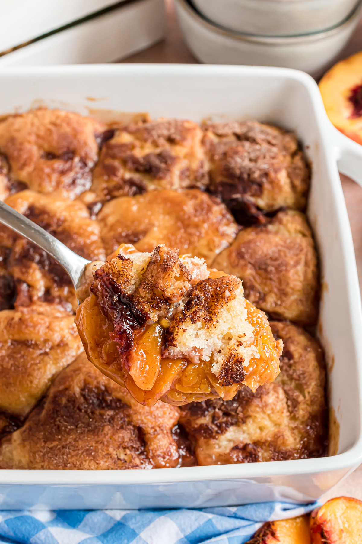 A serving spoon that is full of peach cobbler showing chunks of juicy, sweet peaches and fluffy biscuit topping.