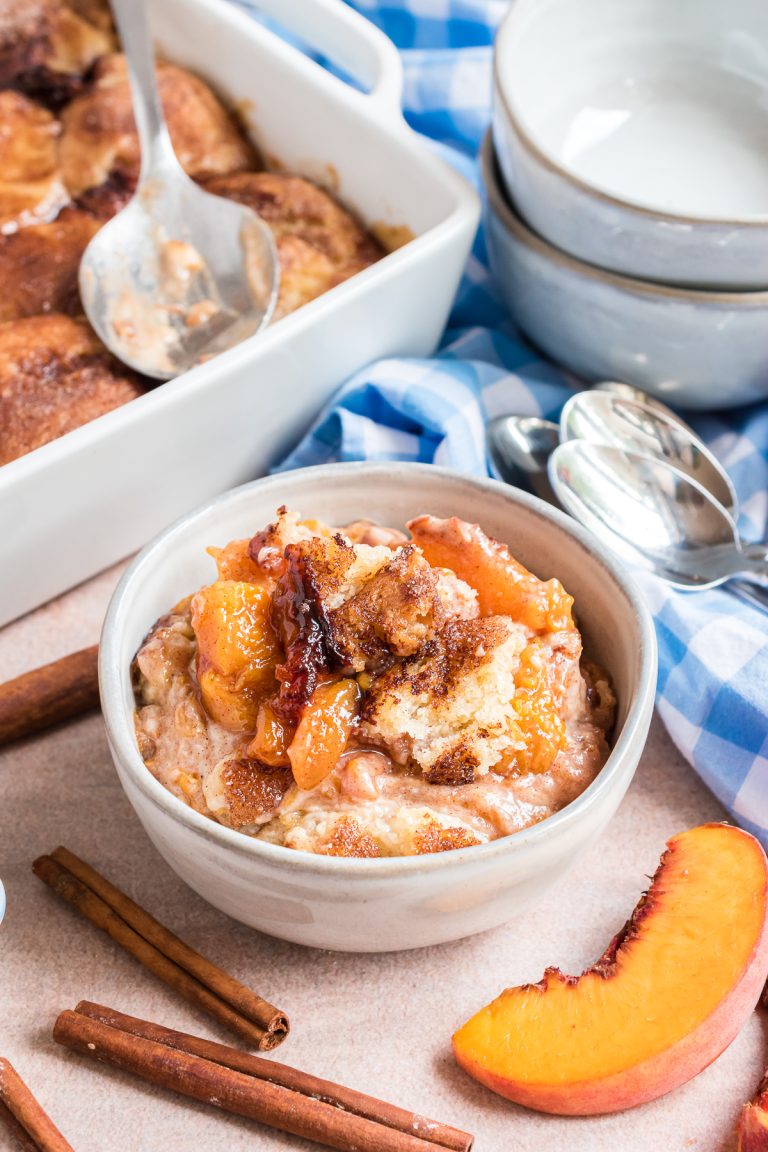 A bowl of peach cobbler topped with biscuits and cinnamon sugar.