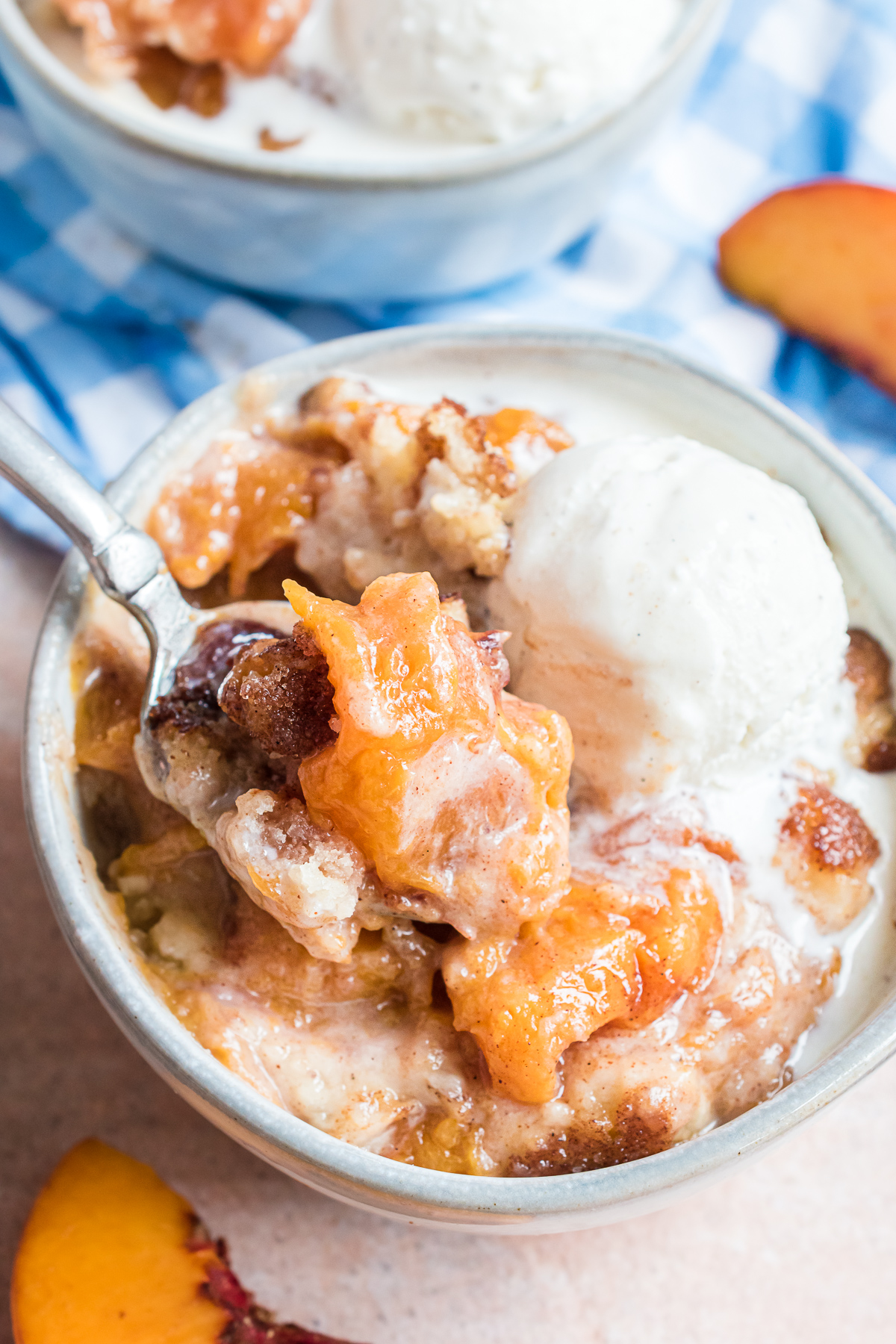 Peach cobbler in a small small bowl with a scoop of vanilla ice cream that is melting over the cobbler.