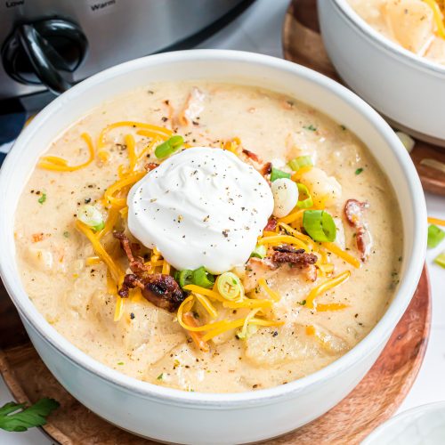 A bowl of loaded baked potato soup topped with sour cream, bacon, and green onion slices.