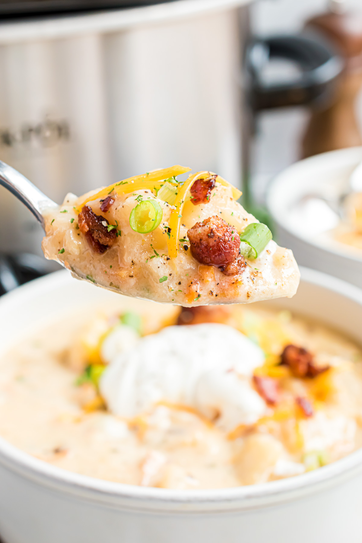 A spoonful of potato soup with bacon bits, green onions and shredded cheddar cheese.