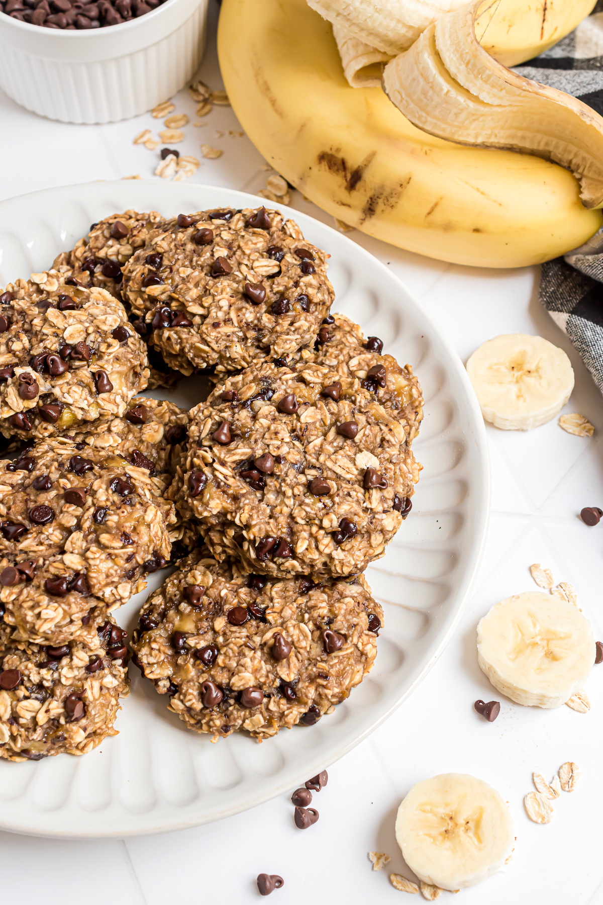 A plate of banana oatmeal cookies with sliced bananas and oats scattered around it.