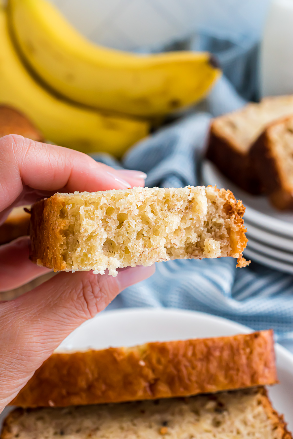 A piece of banana bread is held up to showcase the fluffy and tender, moist texture of the bread.