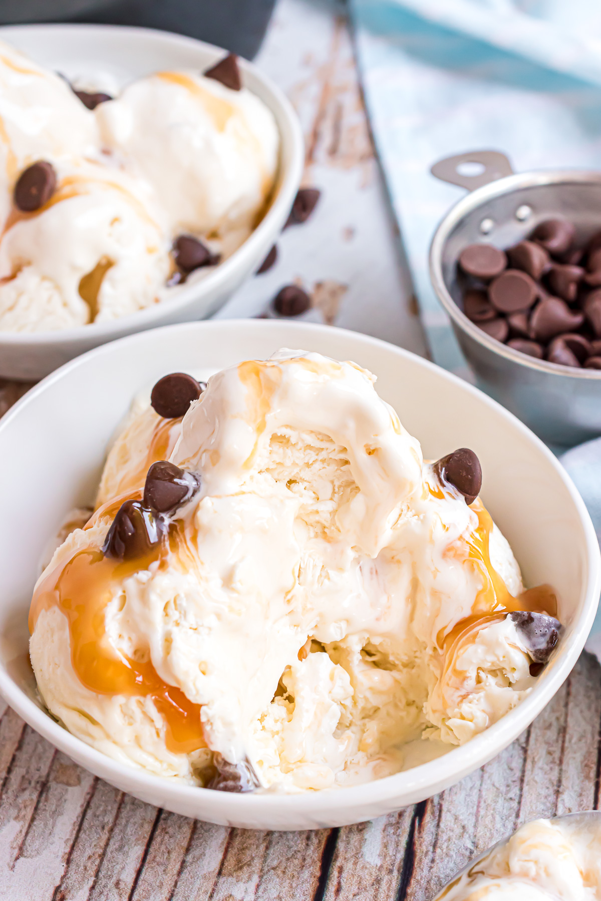 A bowl of sweetened condensed milk ice cream with a large scoop taken out of the side of the serving. The ice cream is drizzled with caramel sauce and chocolate chips.