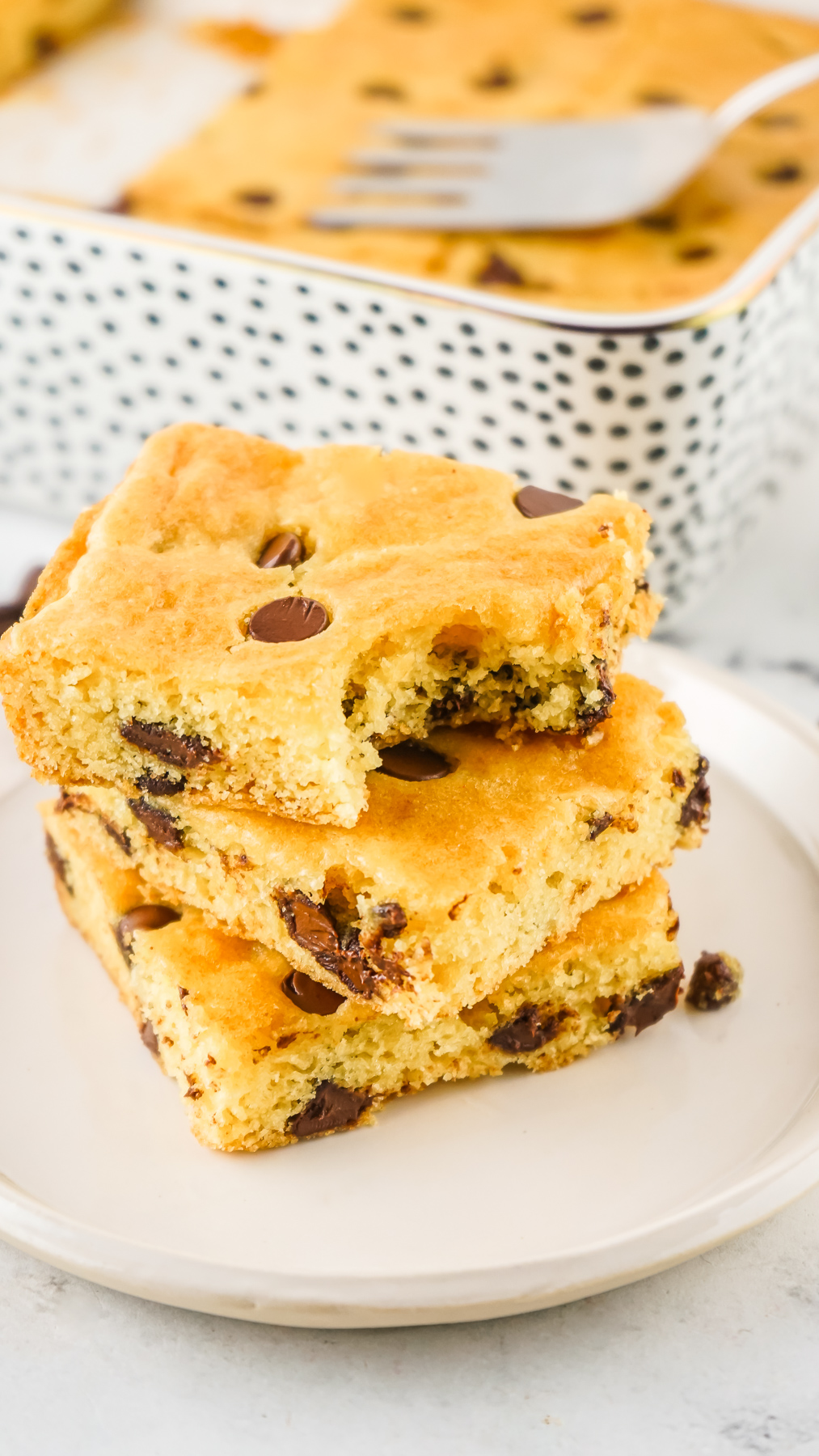 A stack of cake mix cookie bars filled with chocolate chips. The top bar has a bite taken out of it and it's showing the cake-like texture of the cookie.