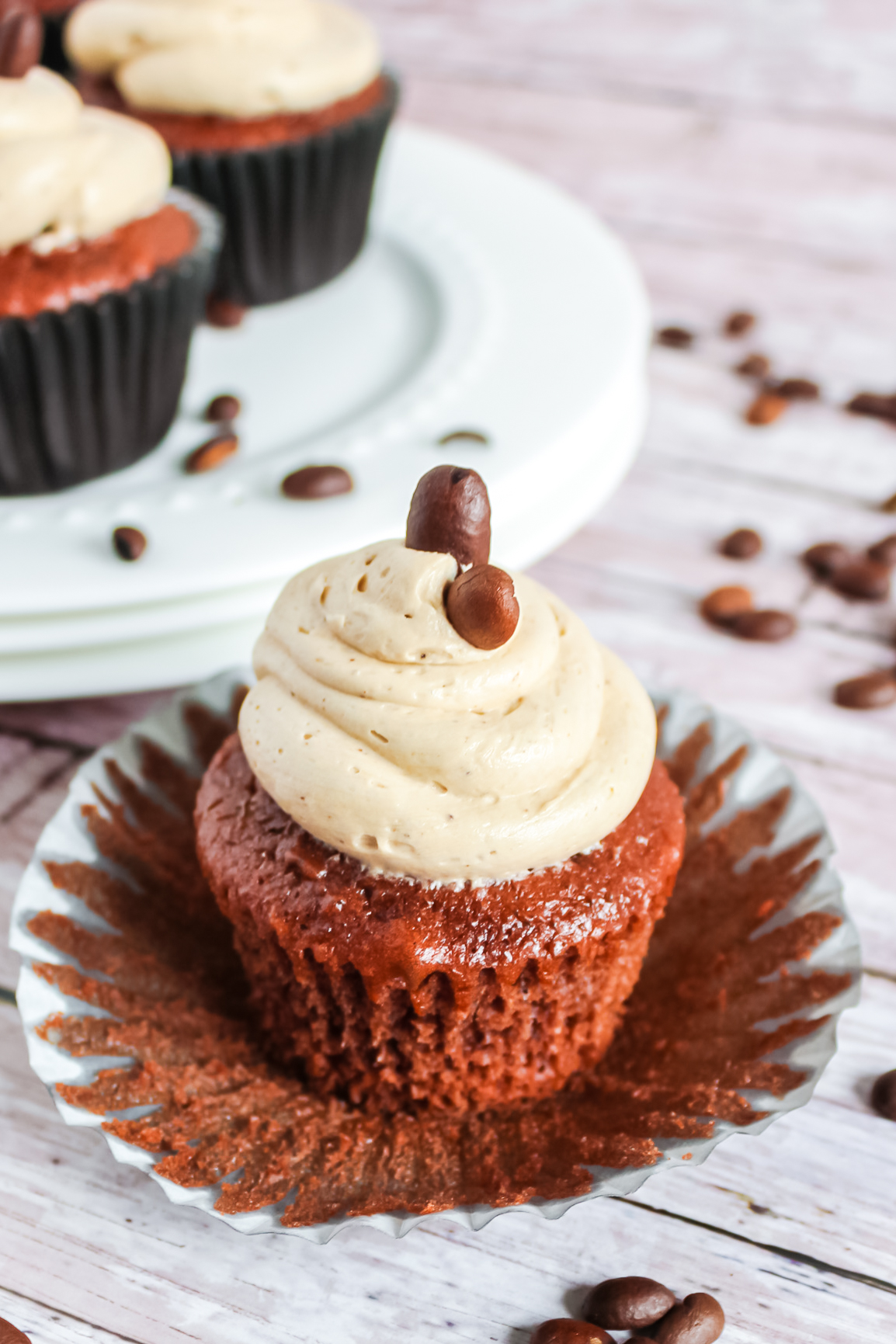 A chocolate cupcake frosted with coffee buttercream sitting on a wrapper exposing the crumb texture of the cupcake.
