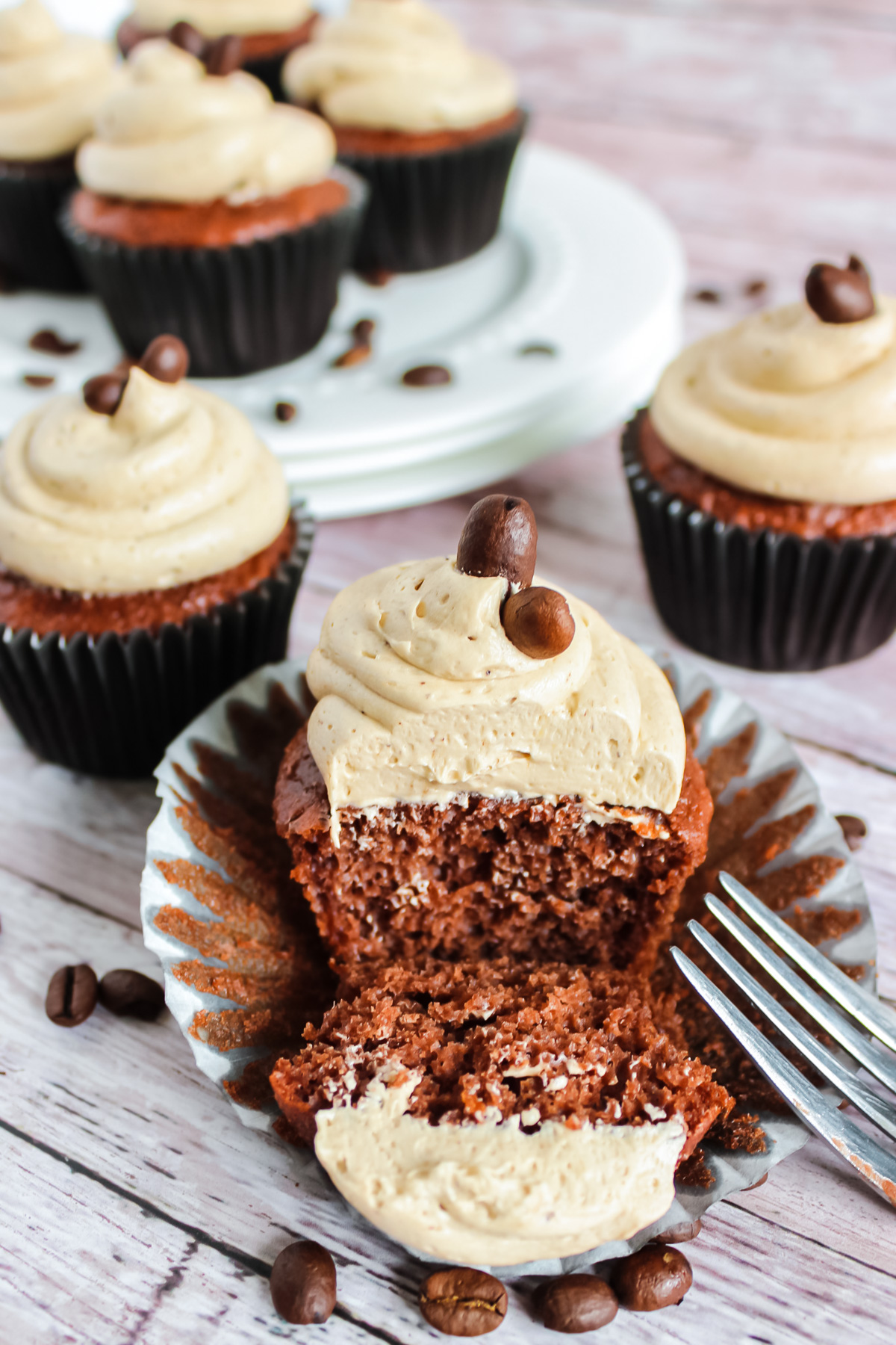 A chocolate cupcake frosted with the best coffee buttercream frosting. The cupcake is cut in half showing the texture of the piped frosting as well as the crumb texture of the cupcake.