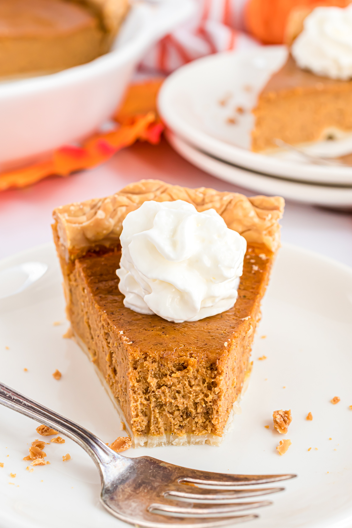 A slice of pumpkin pie with a bite taken out of it with a fork.