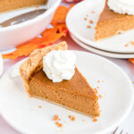A piece of pumpkin pie on a white plate with a dollop of whipped cream on top.