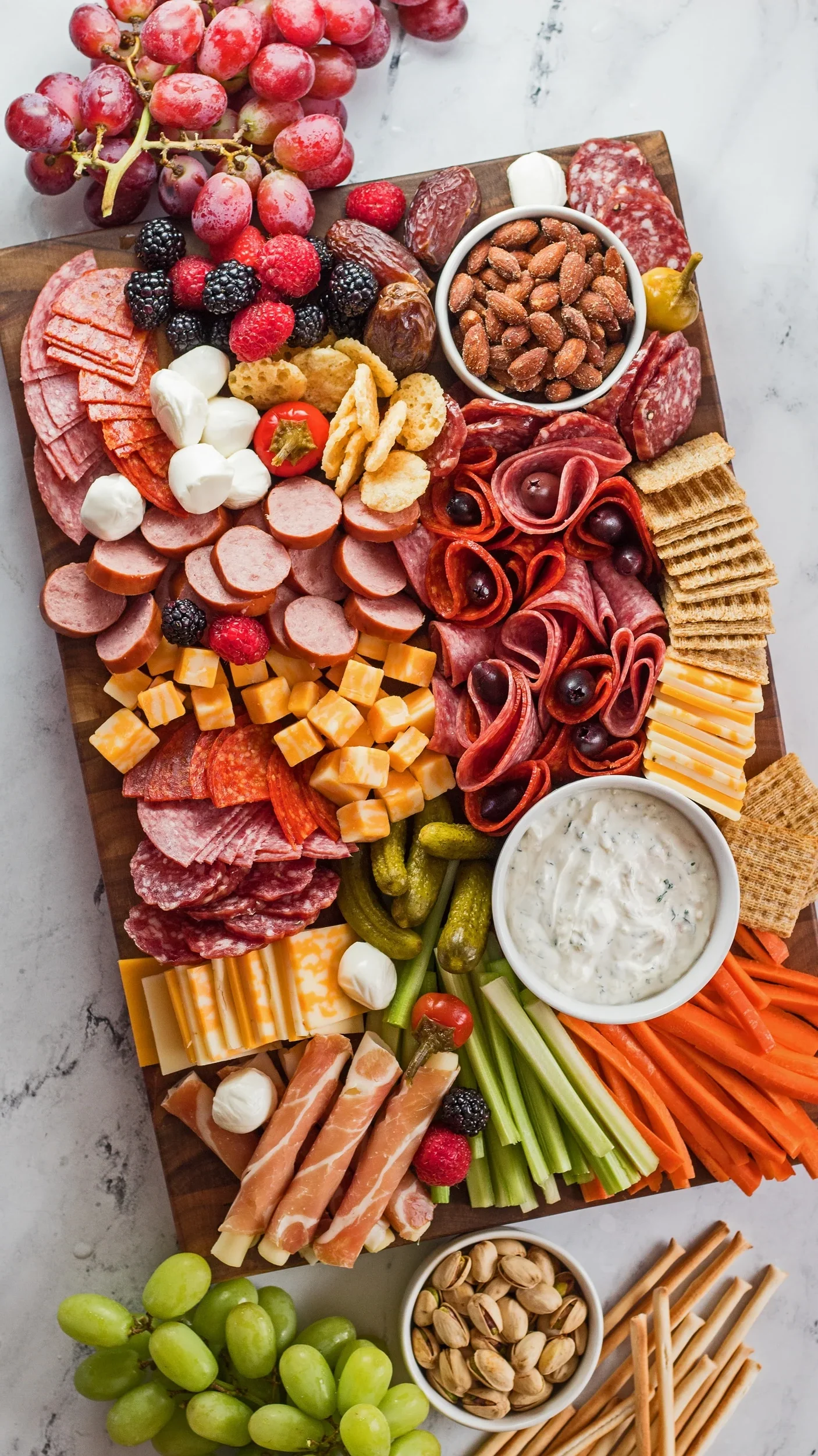 A rectangular meat and cheese board featuring crackers and fresh veggies.