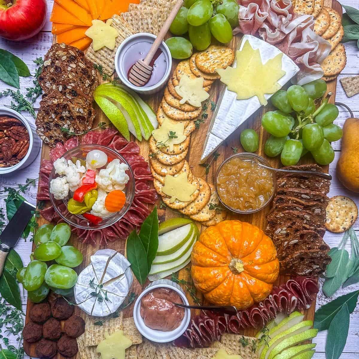 A fall appetizer board with fruits, meats, crackers and jams and jellies.