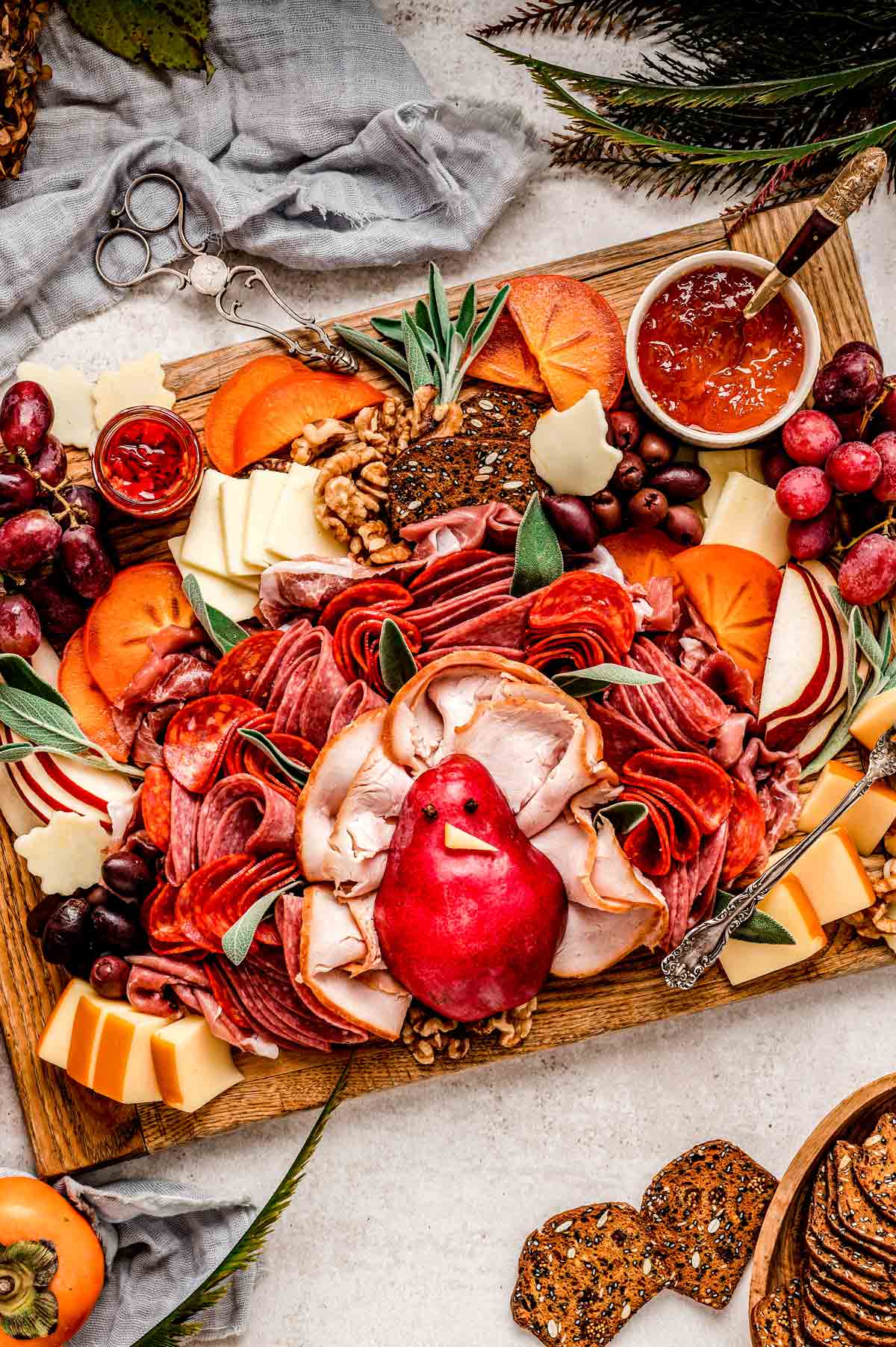 A Thanksgiving charcuterie board that features a turkey made from a pear and feathers made from different folded up meats.