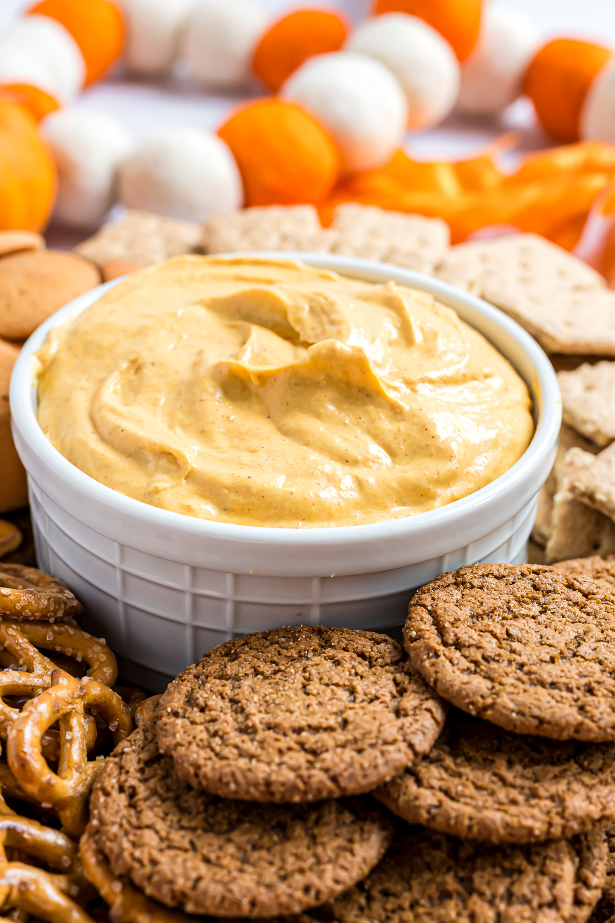 A small serving bowl filled with Pumpkin Fluff surrounded by gingersnap cookies and pretzel twists.