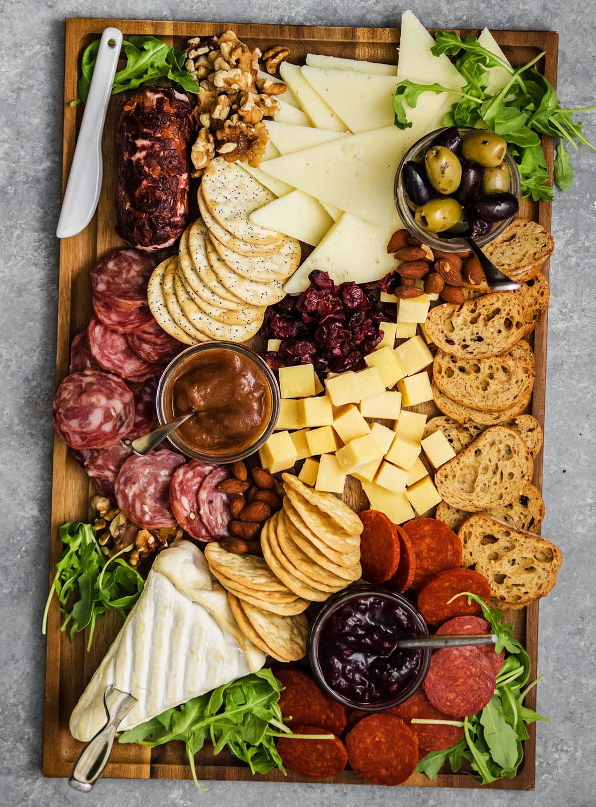 A rectangular meat and cheese board accented by arugula and dried fruit and nuts.