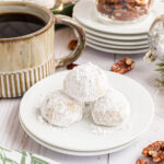 A plate of three snowball cookies with a green mug of coffee and glass jar of pecan sitting in the background.