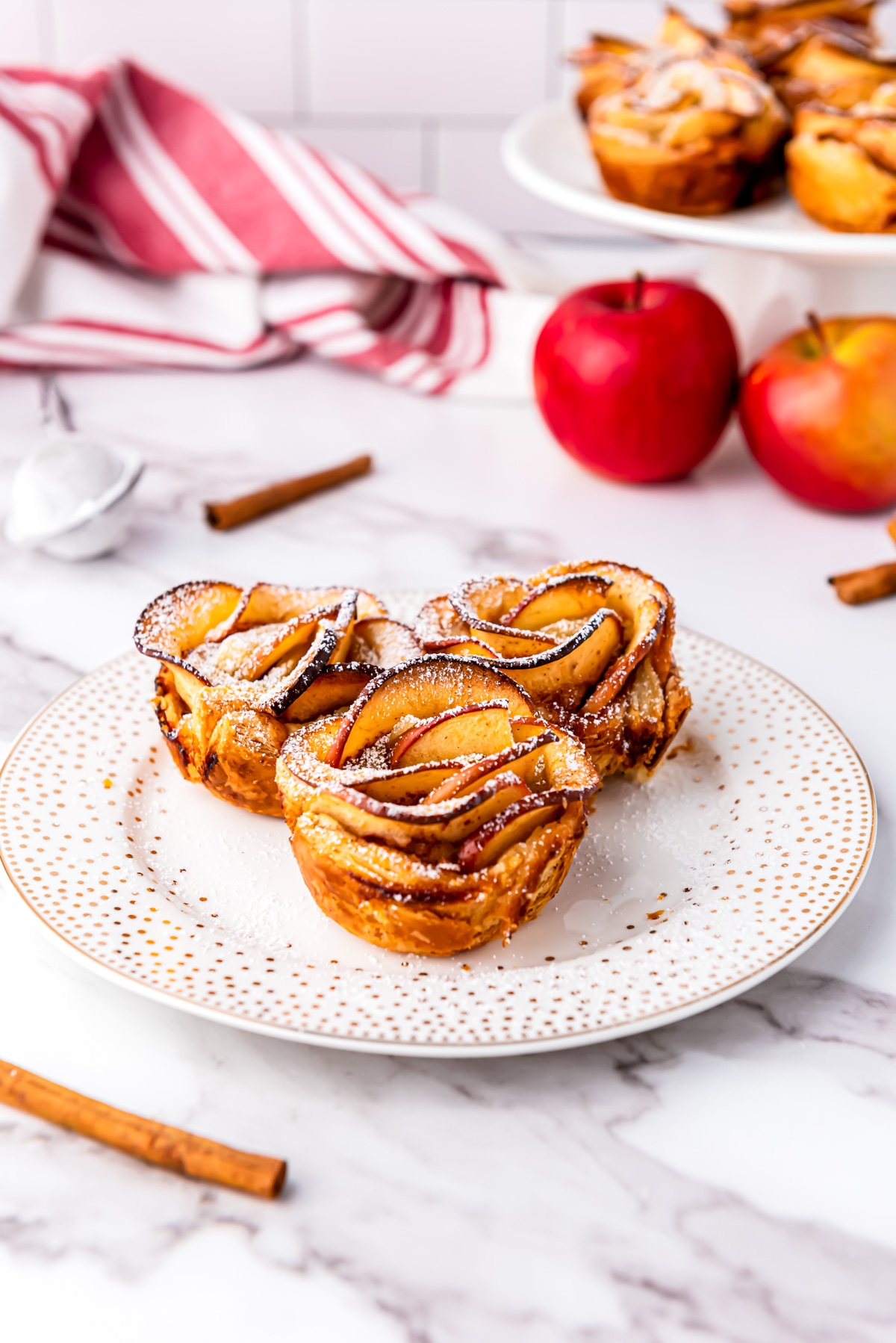 Three Apple Roses with Puff Pastry sprinkled with powdered sugar and sitting on a plate.