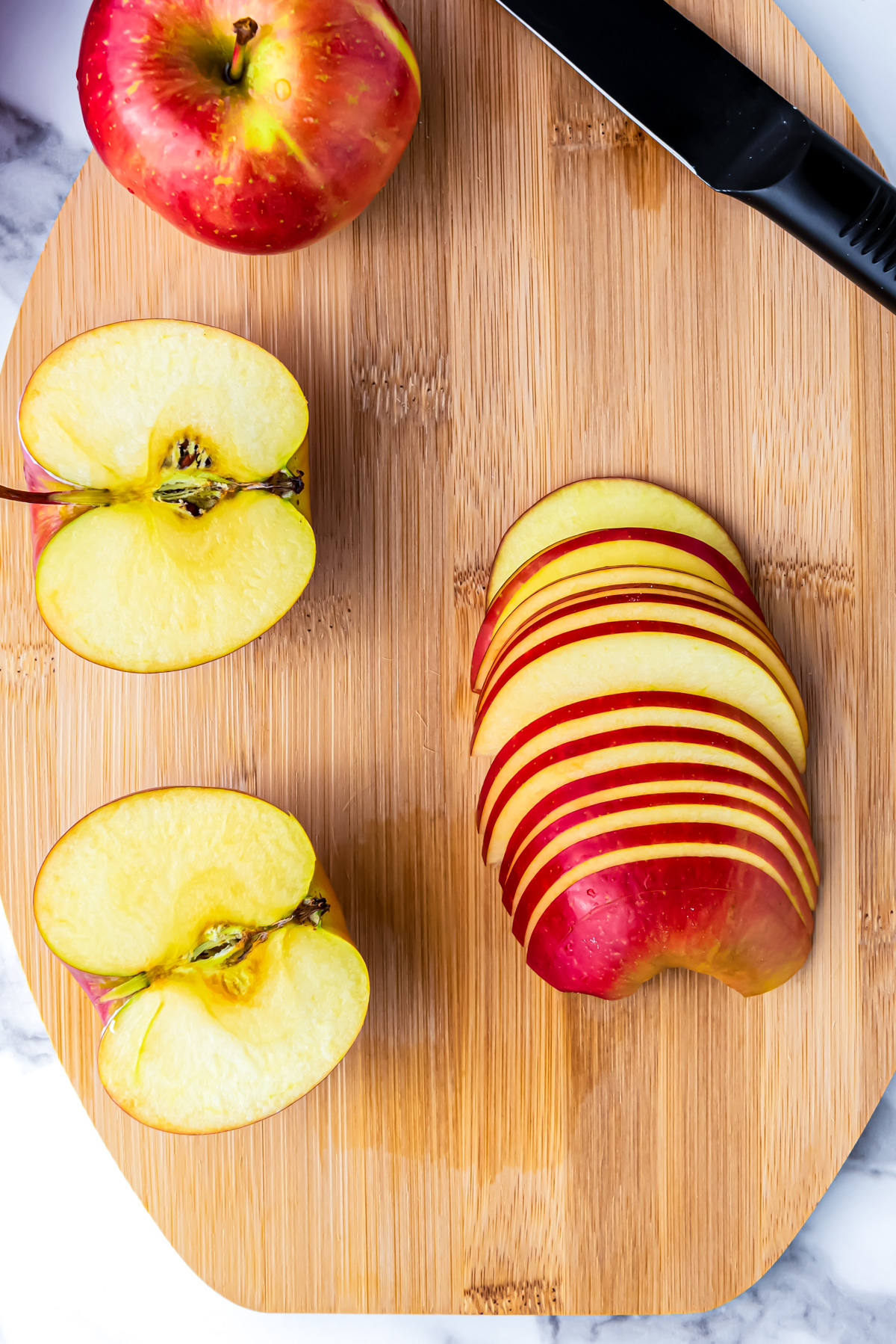 Three apples on a wooden cutting board - 1 whole, 1 cut in half, and 1 cut into very thin slices.