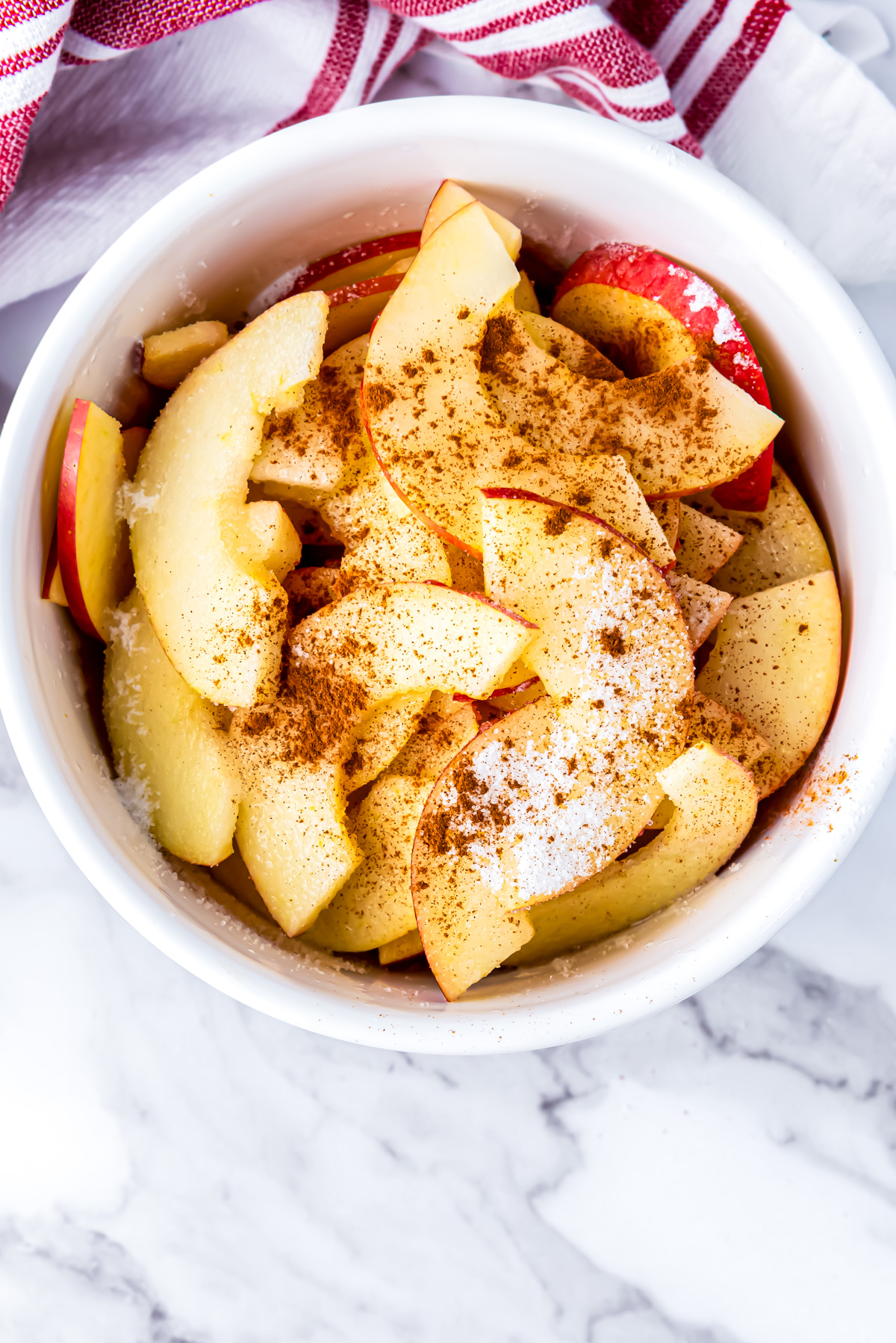 The apple slices in a bowl with the lemon juice and a sprinkling of cinnamon and sugar.