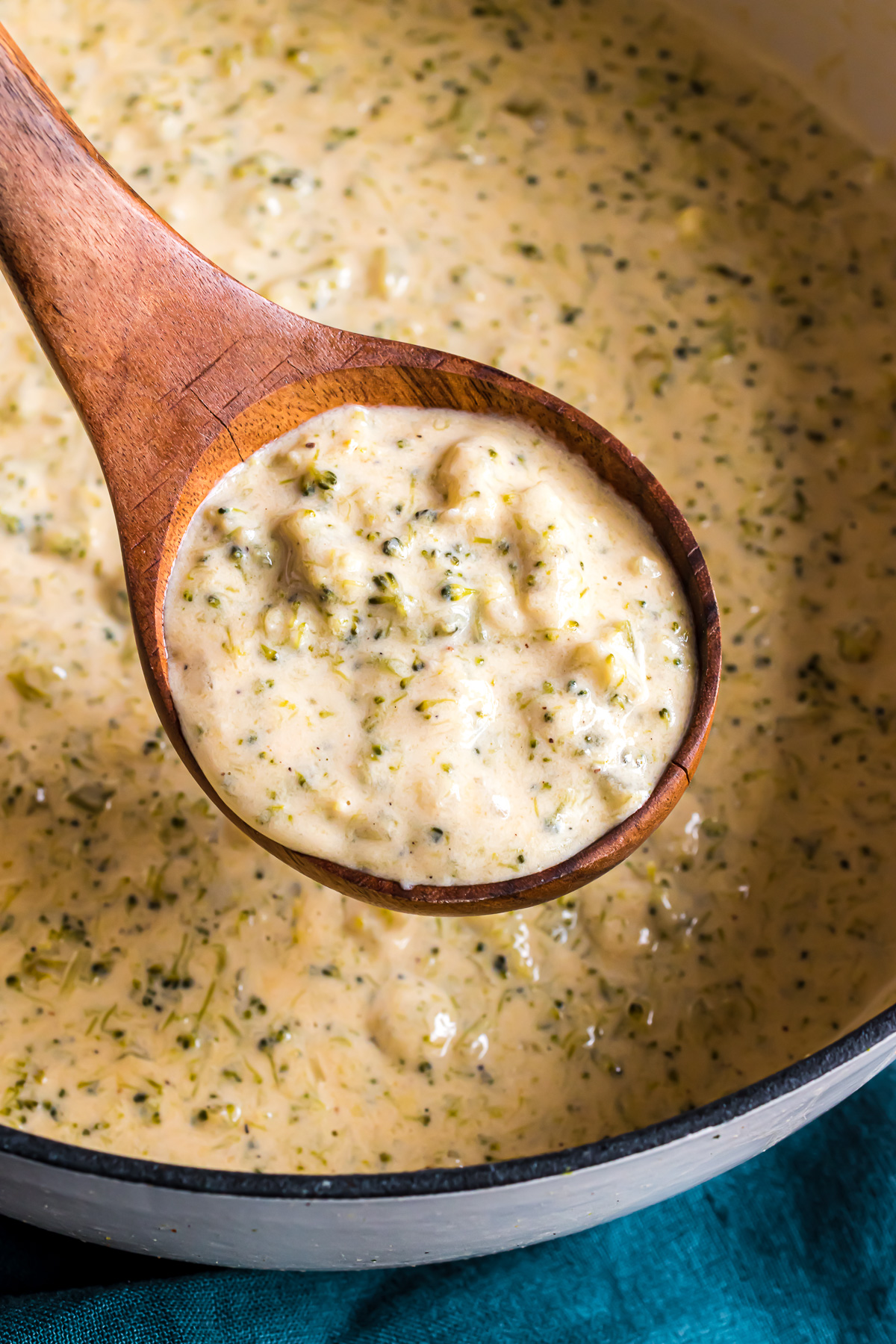 A wooden ladle filled with broccoli cheese soup hovering over the soup pot.