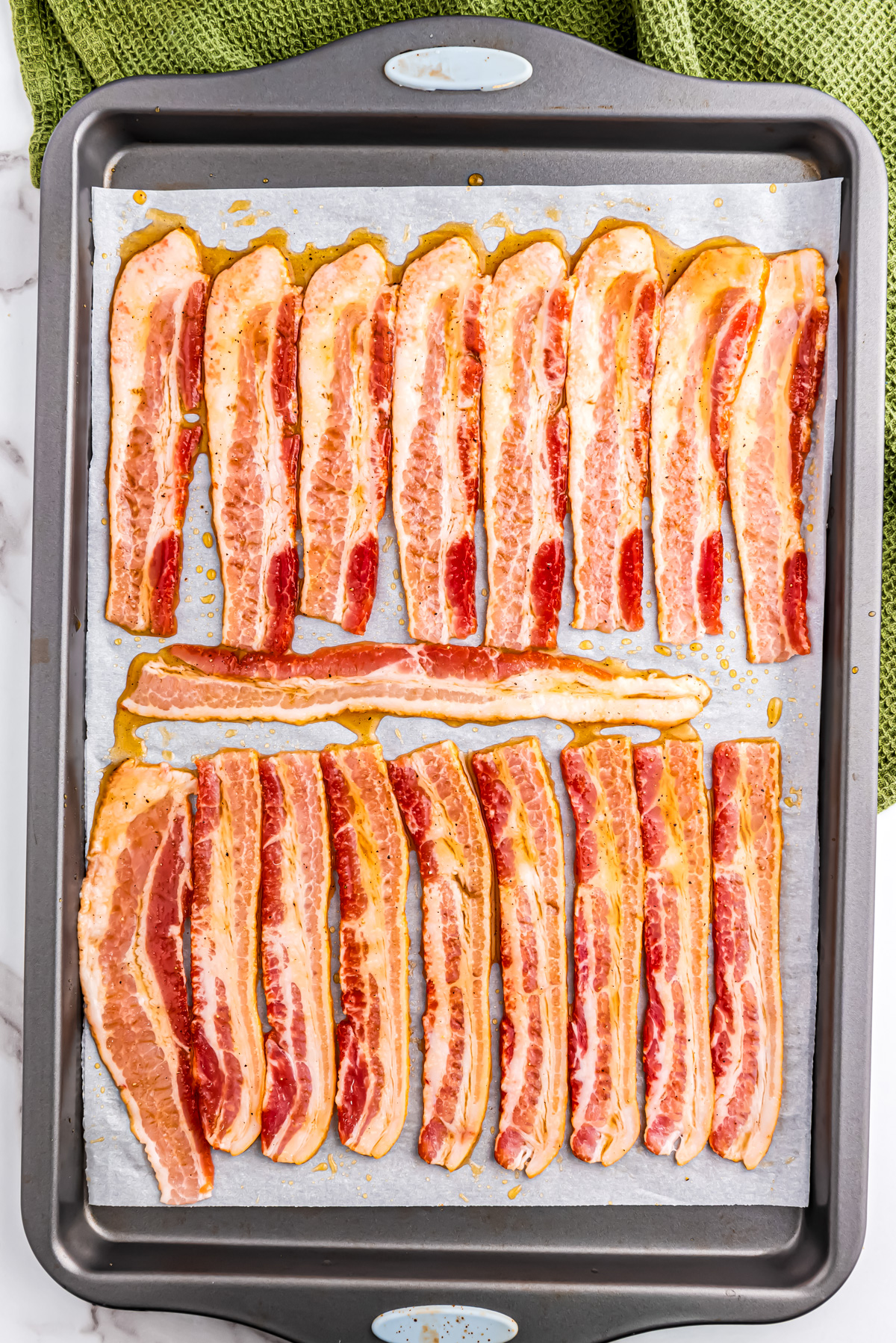 The bacon on a parchment lined tray, covered with maple glaze, waiting to be cooked in the oven.