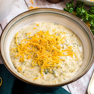 A bowl of broccoli cheese soup topped with finely shredded cheese.