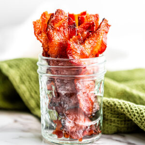 A glass mason jar filled with strips of candied maple bacon.