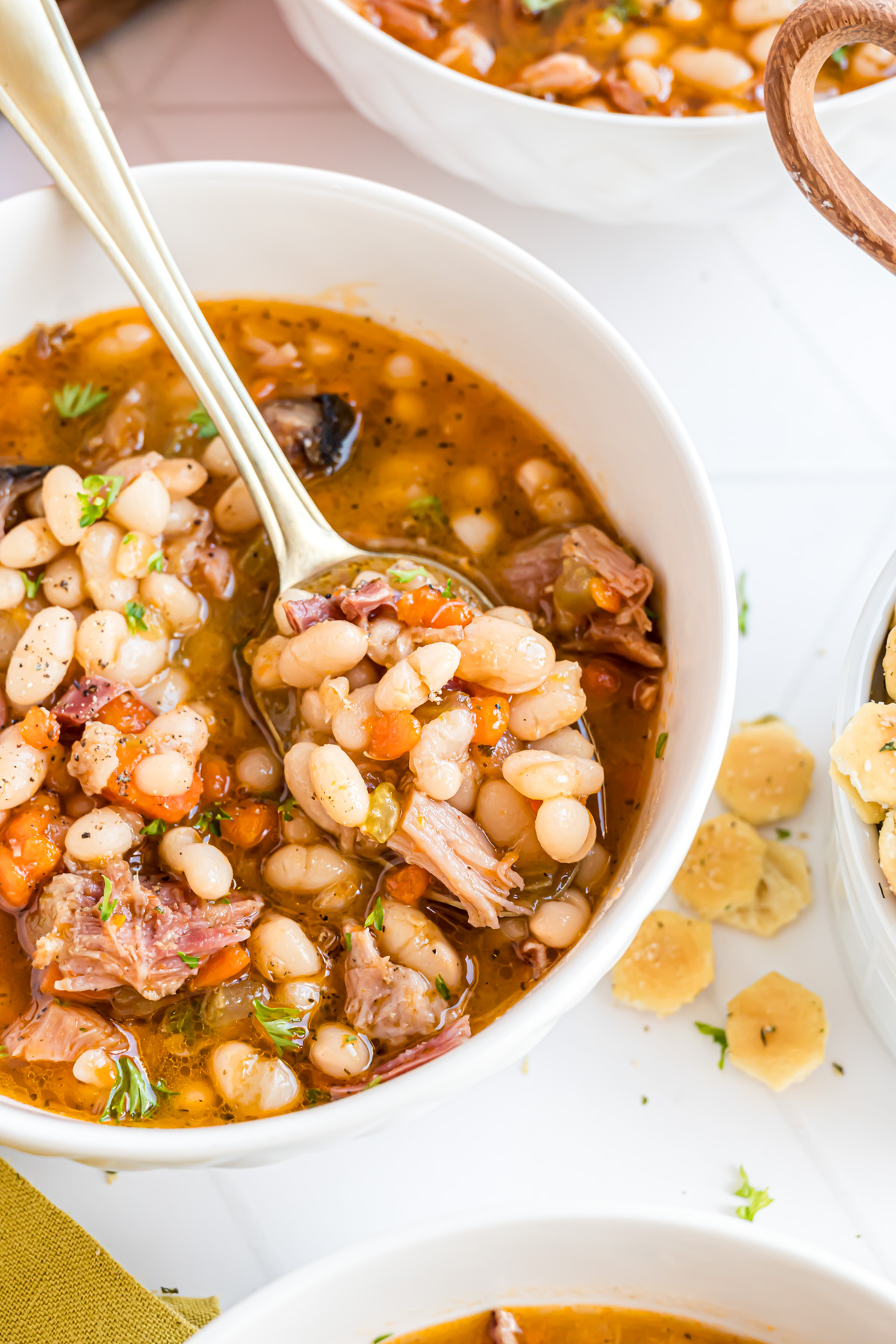 A gold spoon resting on a white bowl  with soup. The spoon is filled with a bite of hearty navy bean soup.