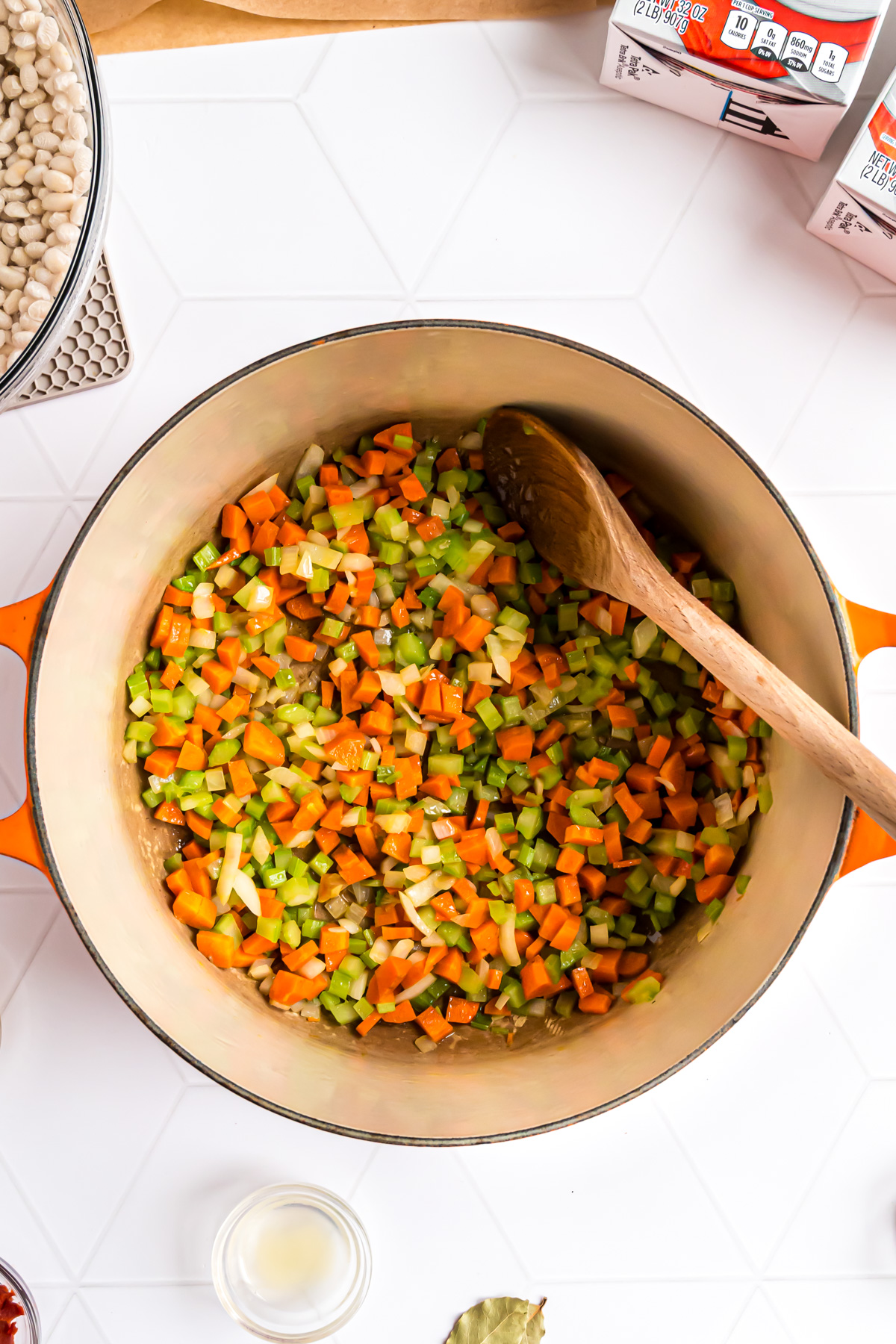 A large Dutch oven with onion, carrots and celery being sauteed in olive oil.