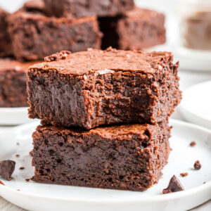 A stack of 2 espresso brownies on a white place. The top brownie has a bite taken out of it.