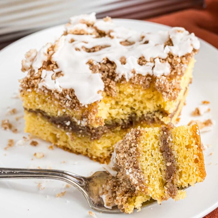 A piece of cinnamon coffee cake on a plate with a bite on a fork.
