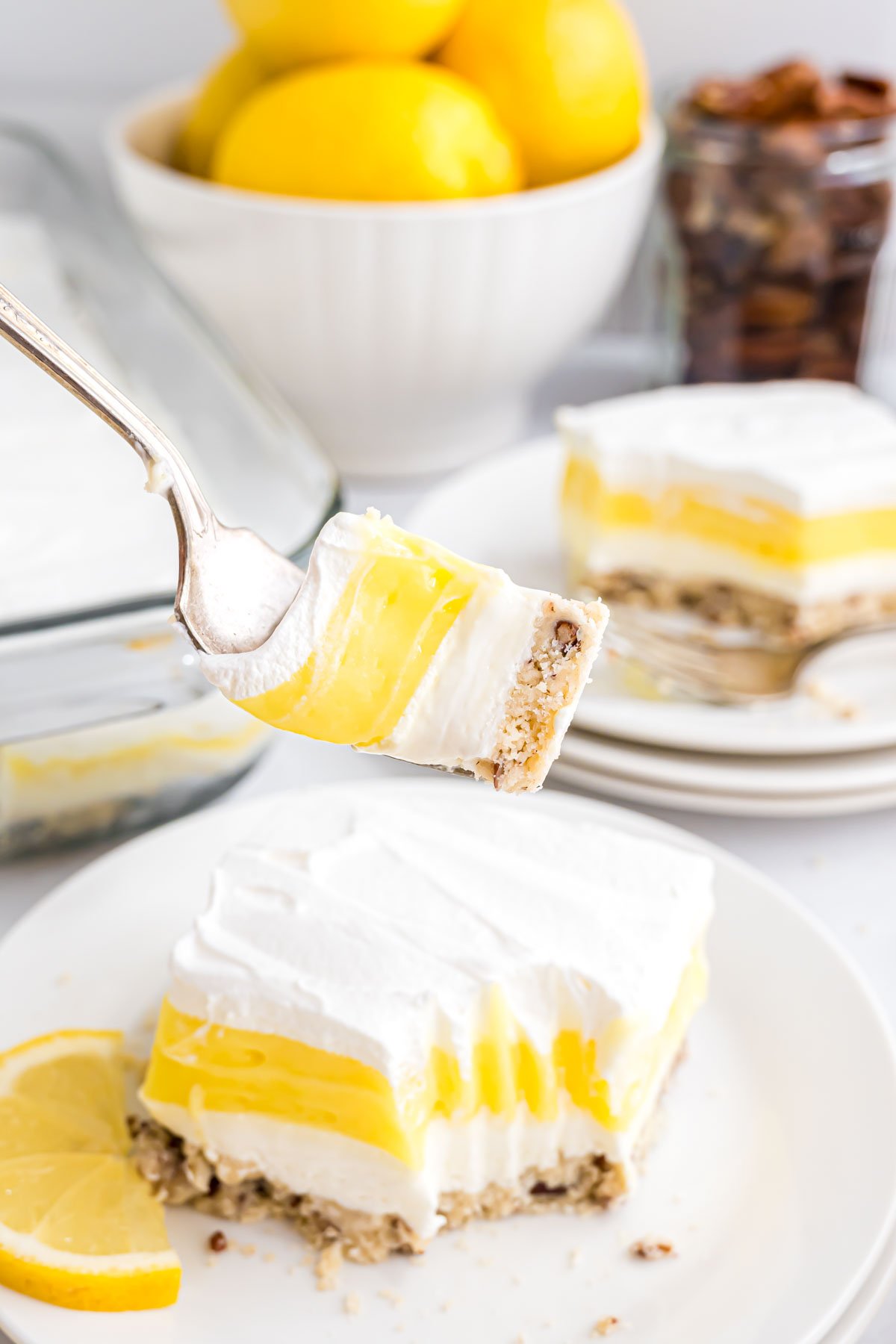 A piece of Lemon Lush on a serving plate with a fork loaded with a bite of dessert on it.