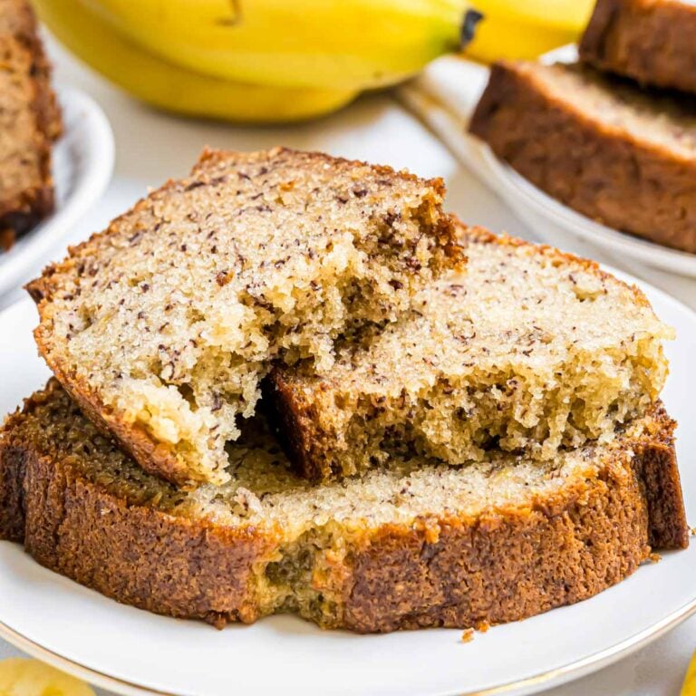 A small plate with banana bread slices on it. The top slice has been broken into two pieces of reveal the texture of the bread.