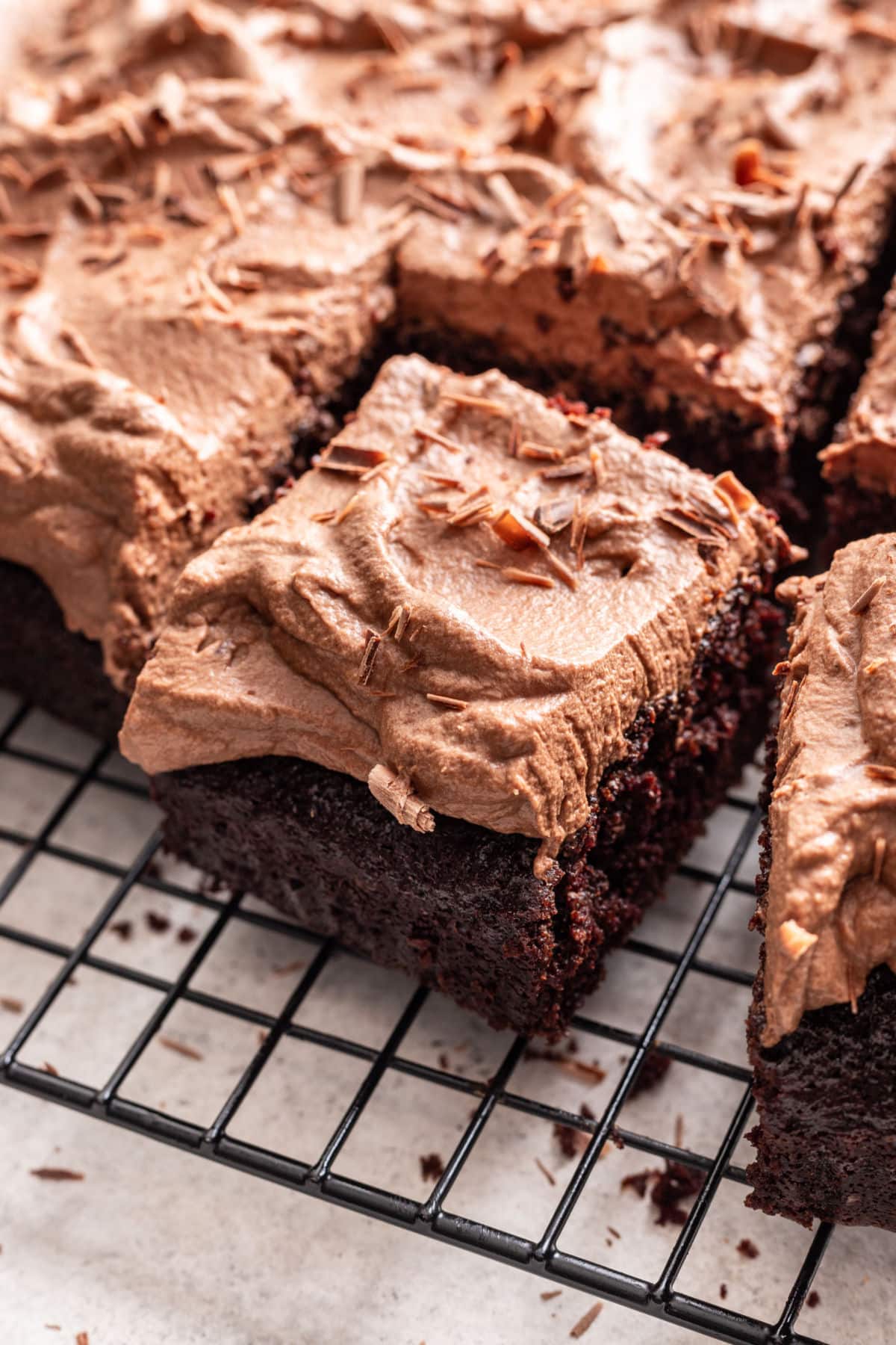 A chocolate cake topped with chocolate marshmallow mousse, cut into squares on a cooling rack.