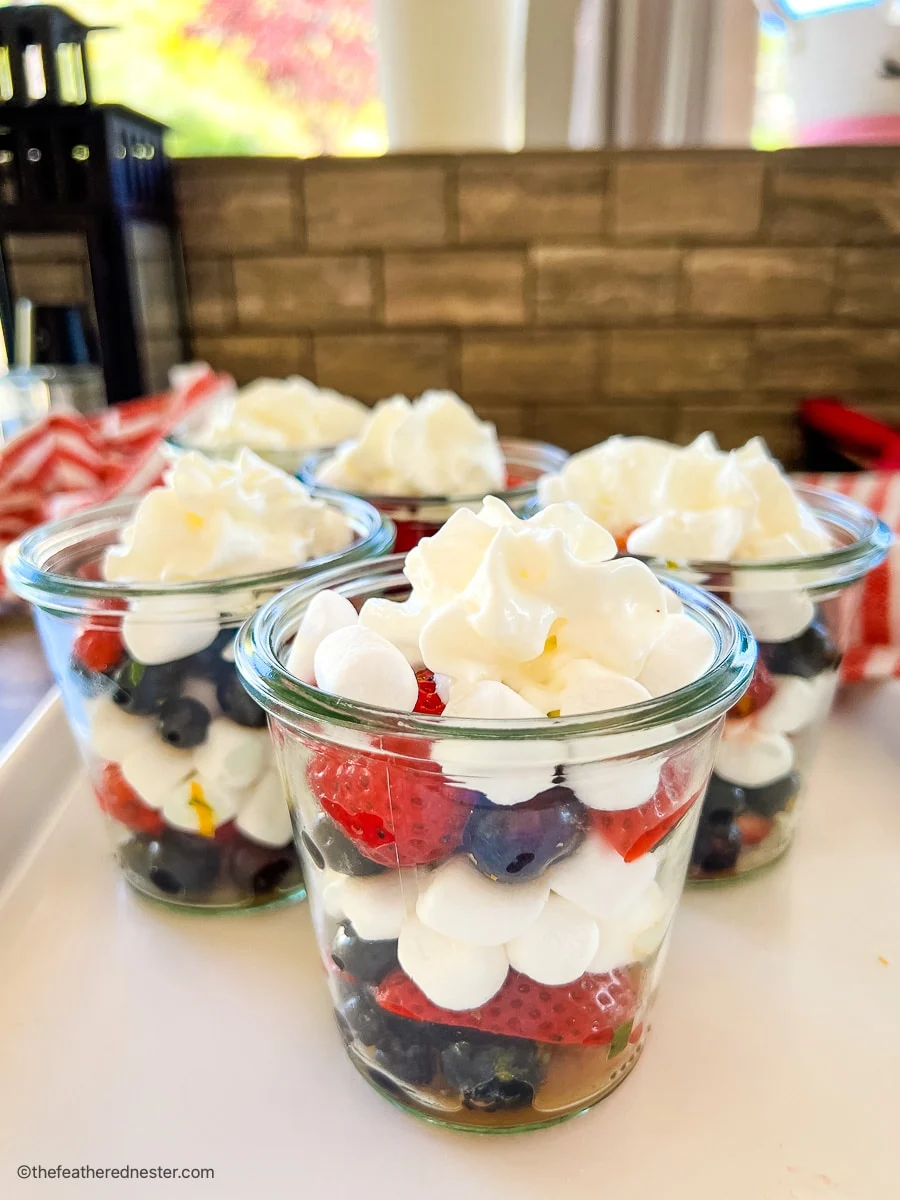 Glass jars with a layered fruit salad featuring strawberries, blueberries, marshmallows and whipped cream.