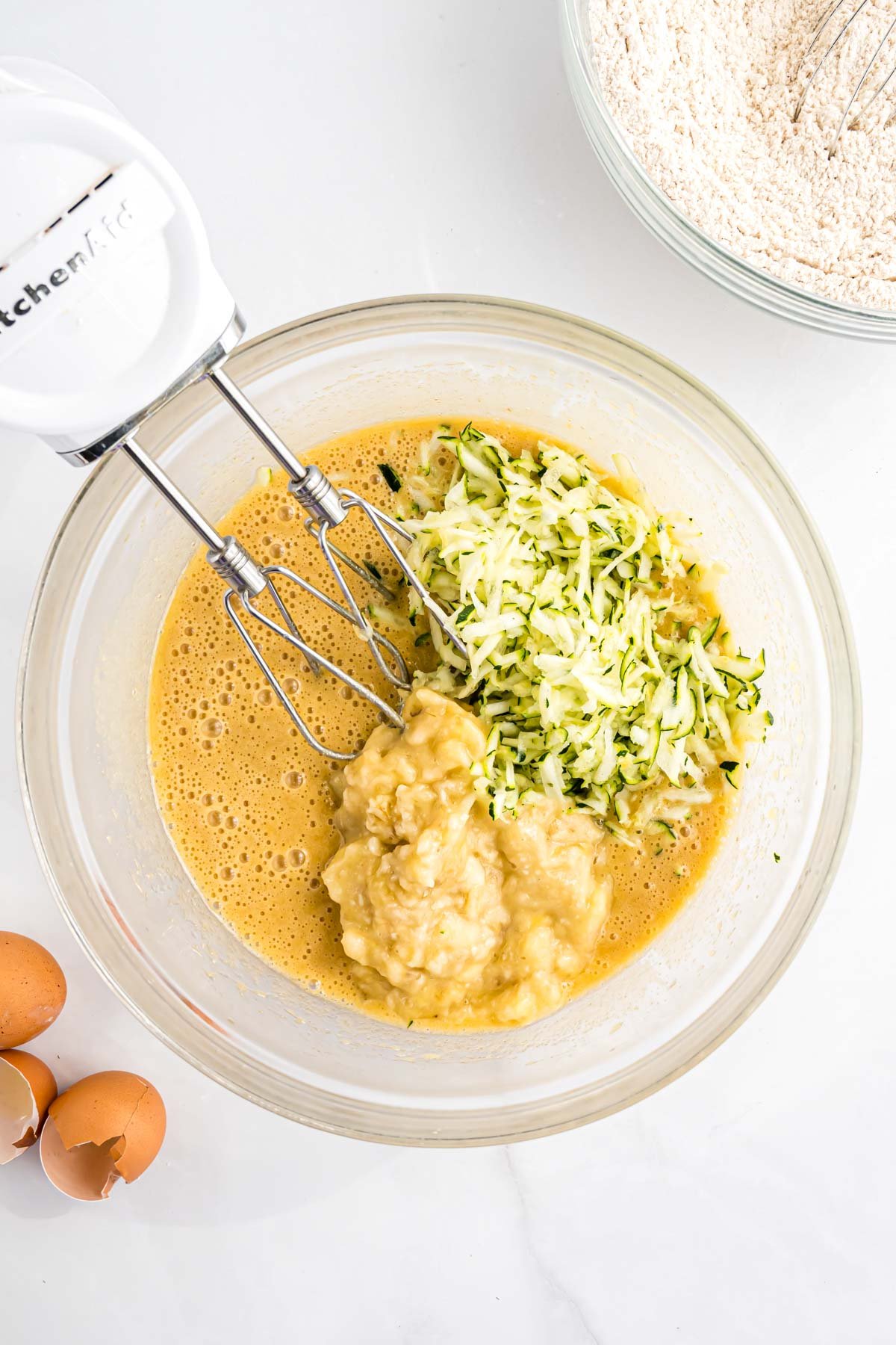 The wet ingredients for the bread, including the shredded zucchini and mashed banana, in a large mixing bowl.