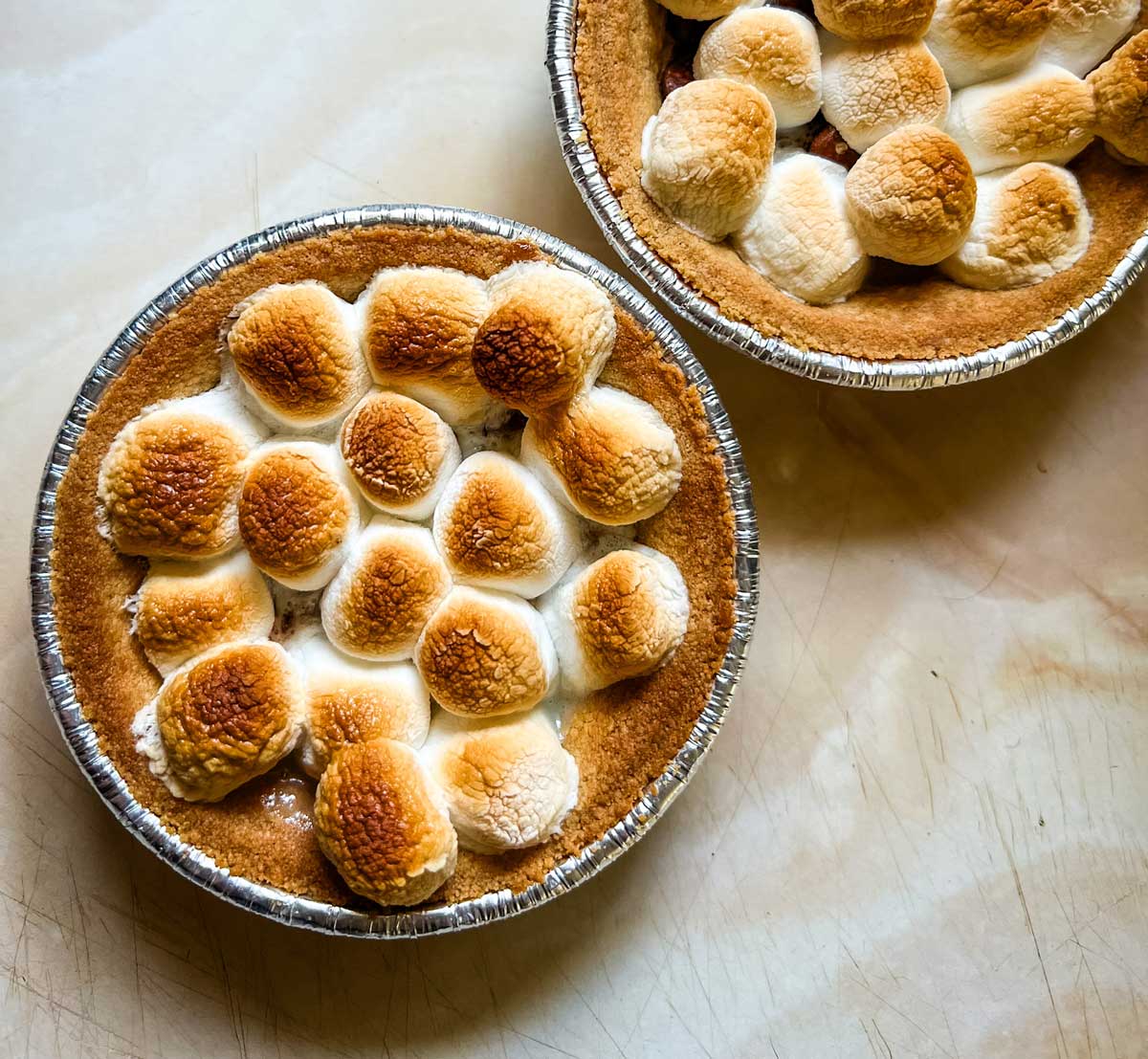 Mini s'mores pies in tins with toasted marshmallows on top.